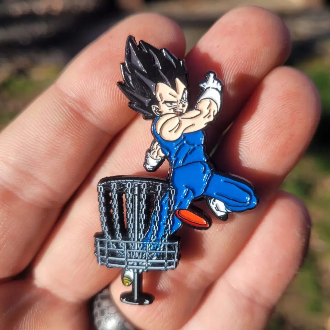 A person holding up a pin with a dragon ball z character on it.