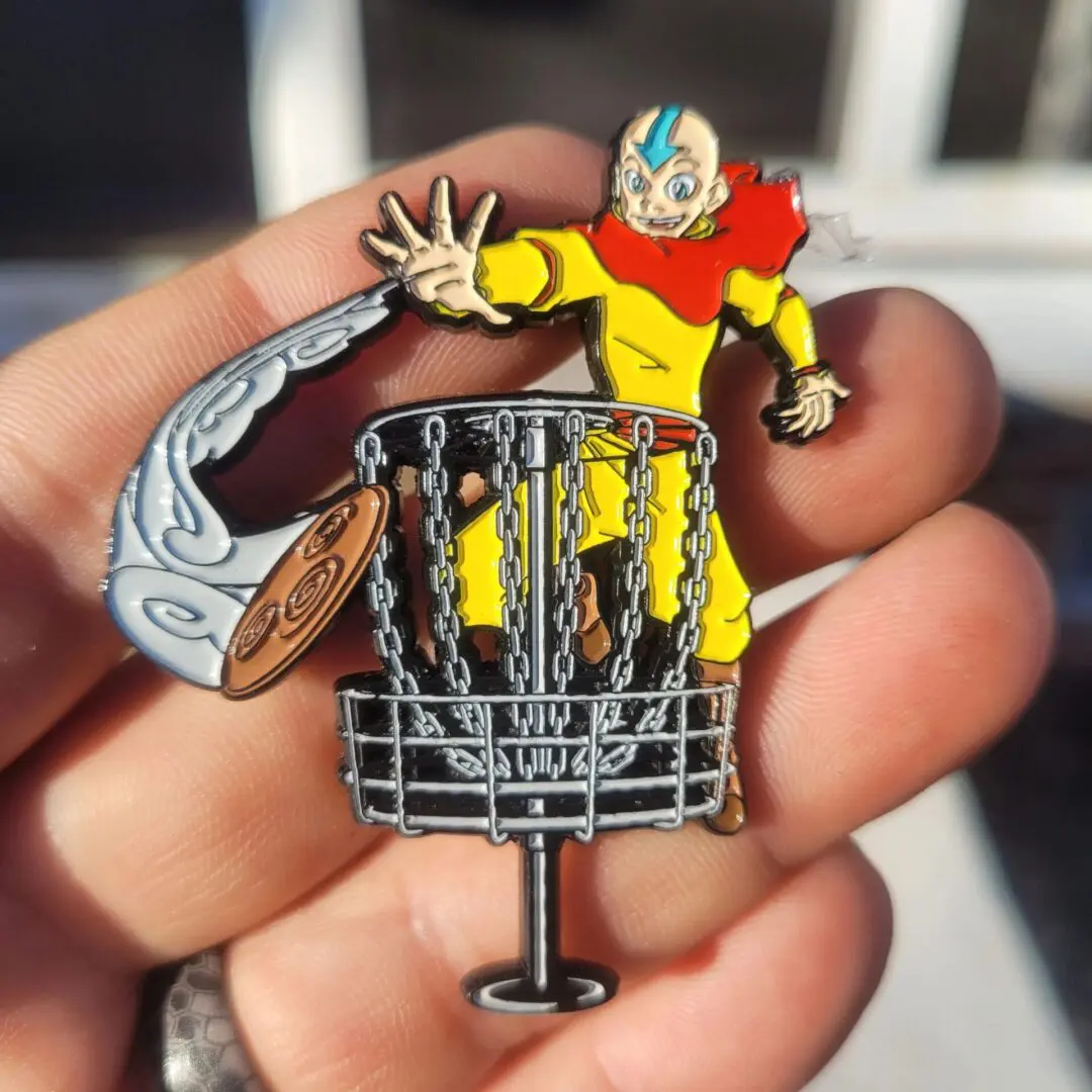 A person holding up a pin with a cartoon character on it.