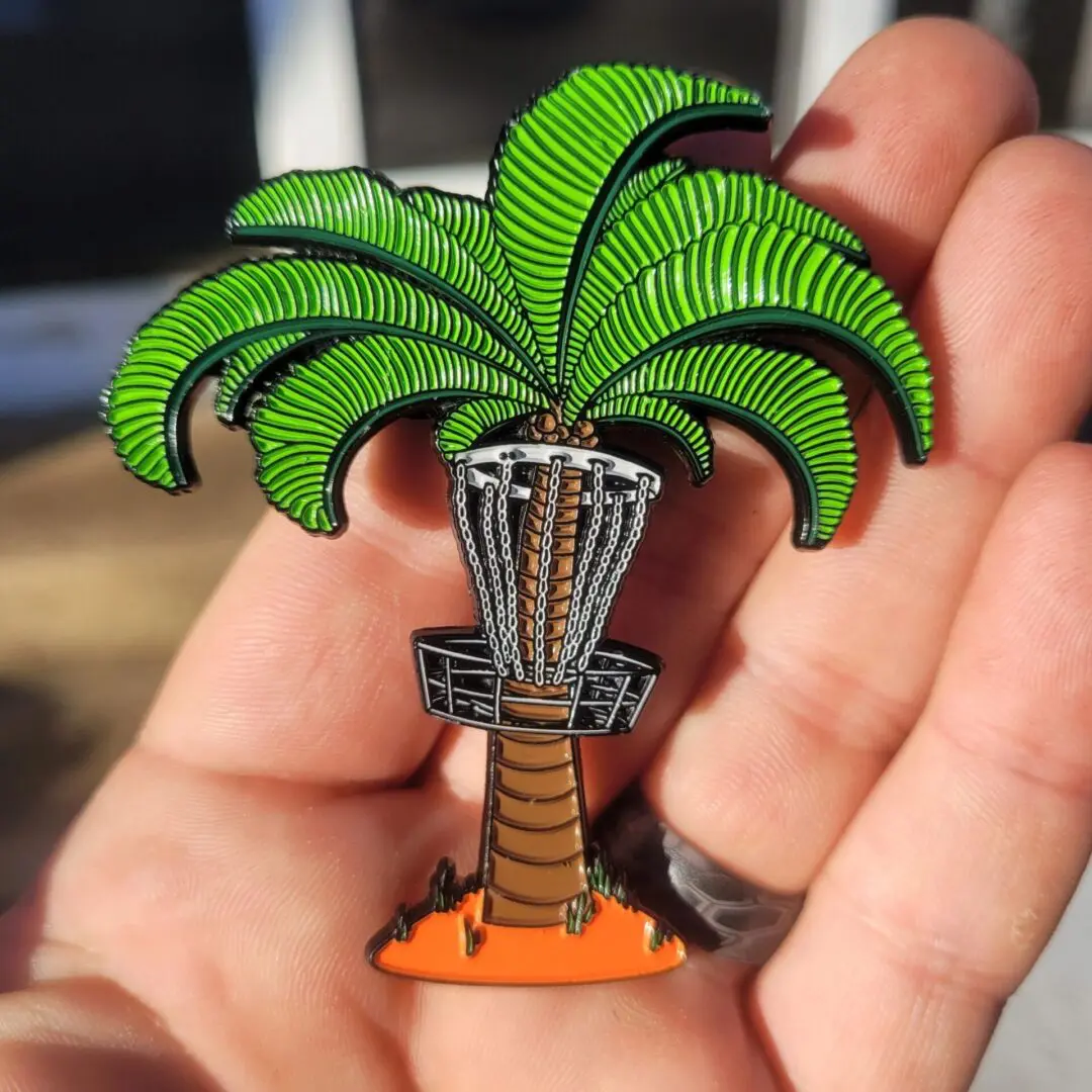 A palm tree pin is held in someones hand.