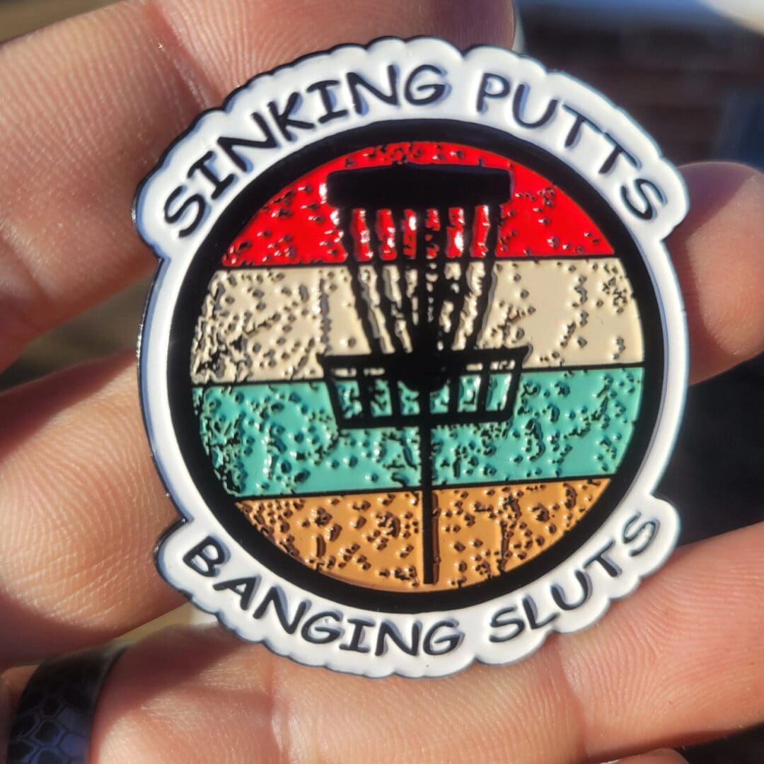 A person holding a patch that says " sinking putts, banging sluts ".