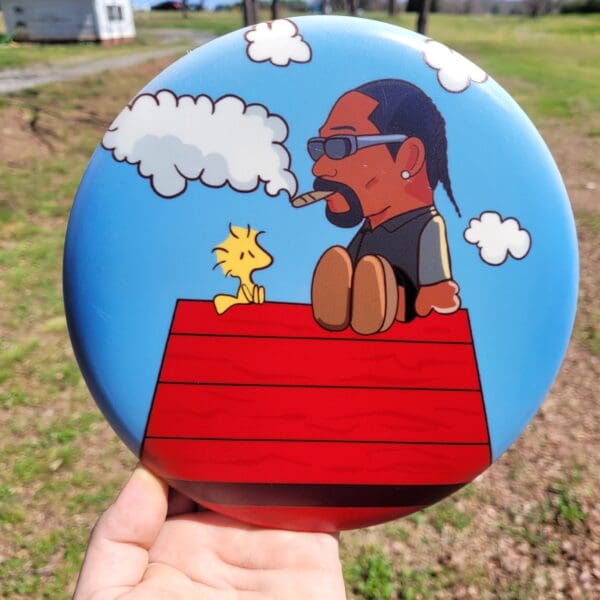 A hand holding up a frisbee with snoop dogg on it.